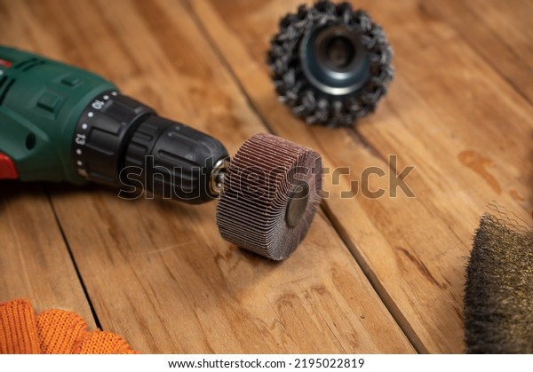 Electric drill, flap wheel,\
knot bowl wire disk, metal brush against the wooden background.\
Electric and hand tools for woodworking. Indoors. Selective\
focus.