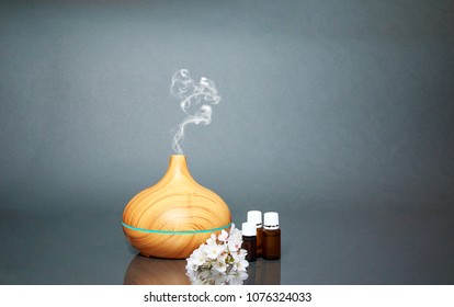 Electric Essential oils Aroma diffuser, oil bottles and flowers on gray surface with reflection. - Shutterstock ID 1076324033