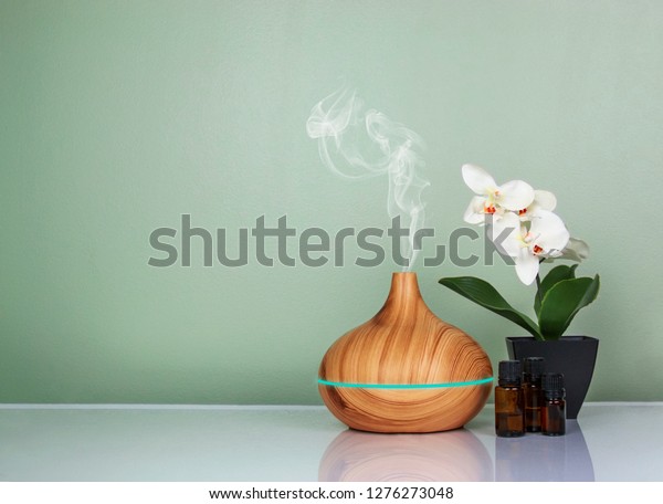 Electric Essential oils\
Aroma diffuser, oil bottles and flowers on light green surface with\
reflection.