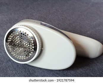 Electric Fabric Shaver On A Gray Sweater. Used To Remove Fabric Fluff, Fuzz, Bobbles, Pills Or Burr From All Types Of Garments And Fabrics. Helps To Restore Clothes And Fabrics To A Fresh New Look.