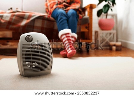 Electric fan heater on the floor in living room with human sitting on the sofa at background