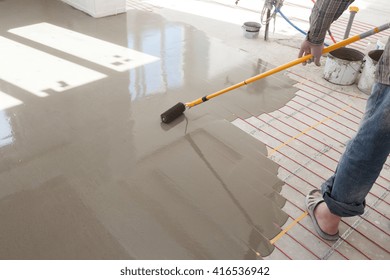 Electric Floor Heating System Installation In New House.Worker Use A Roller For Pouring Concrete Floor