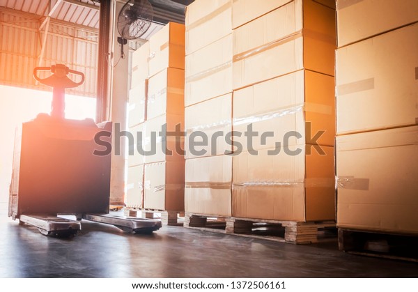 Electric forklift  or hand pallet jack and\
stack of cardboard boxes on wooden\
pallet.