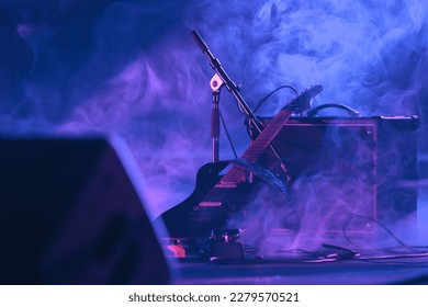 
				electric guitar with its an amp in the dark on the stage of a concert with smoke and blue and pink lighting