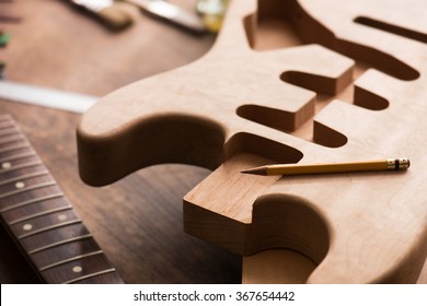 Electric guitar making. Guitar work shop. Unfinished solidbody electric guitar body on work bench. Focus is on pencil. Shallow depth of field.  