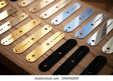 Electric Guitar Metal Parts And Wood On Work Bench. Gold, Chrome And Black Control Plates For Electric Guitar Aligned For Assembly.