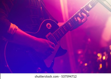 Electric guitar player on a stage with colorful blue and purple scenic illumination, soft selective focus
