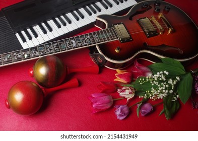 Electric guitar, synthesizer keyboard, maracas and a bouquet of tulips and lilies of the valley on a red table.