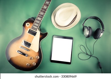 Electric guitar with tablet, hat and headphones on green background - Powered by Shutterstock