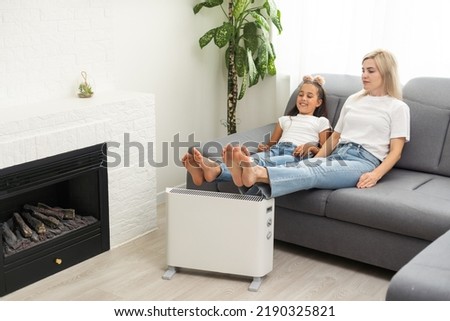 Electric heater at home. Young family warms his frozen hands near a heating radiator