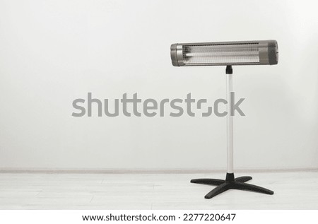 Electric infrared heater on floor near white wall indoors, space for text