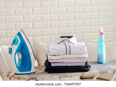 Electric Iron With Folding Cloth, Black Slack Trouser And Spray Starch On The Ironing Board With White Brick Wall Background.