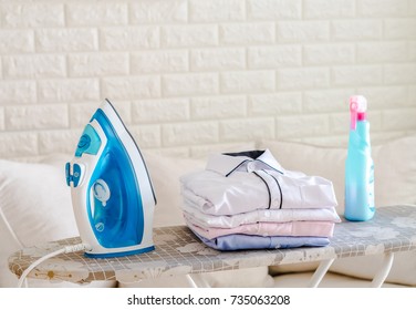 Electric Iron With Folding Cloth And Spray Starch On The Ironing Board With White Brick Wall Background.