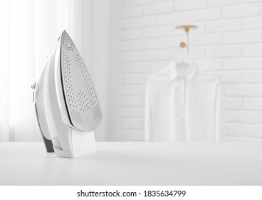 Electric iron on table in blurred room with clothes rack - Shutterstock ID 1835634799