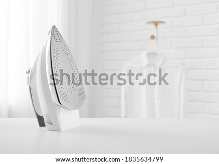 Electric iron on table in blurred room with clothes rack
