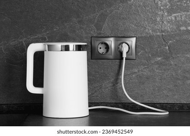 Electric kettle plugged into power socket on dark grey wall indoors - Shutterstock ID 2369452549