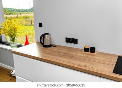 An electric kettle standing on the countertop on the kitchen cabinets visible a large window in the dining room and red vase with goldenrod. - Powered by Shutterstock