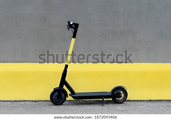 Electric kick scooter in urban environment
against wall, scooter rental, freedom of movement. Electric bike in
the city. Trendy color of the year 2021. Ultimate grey and
illuminating yellow.