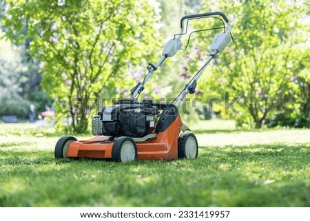 Electric lawn mower for cutting grass on courtyard in private house in summer. Gardening, working in garden. Obligation of home owners to mow lawns concept. Maintenance cleaning of house territory.