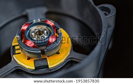 Electric motor rotor with permanent magnet, copper wire inductors and metal ball bearing. Close-up of disassembled computer fan with integrated Hall-effect sensor. Detail of open black plastic cooler.