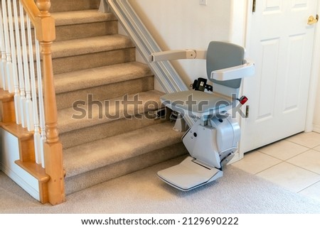 An electric, motorized chair lift for persons with disabilities on a carpeted staircase in a residential home.