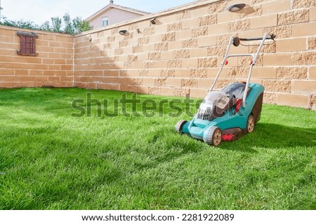 Electric mower machine trimming green lawn of home garden. Backyard lawn maintenance concept.