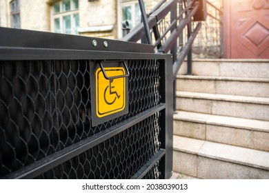 Electric platform lift at building staircase for disabled people with wheelchair sign plate on old city street. Elevator stairlift ramp mechanism for senior disability people. Medical urban equipment