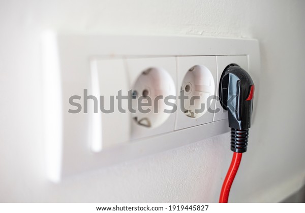 Electric plug. Electric socket. Black power cord cable\
plugged into european wall outlet on white plaster wall with copy\
space. 