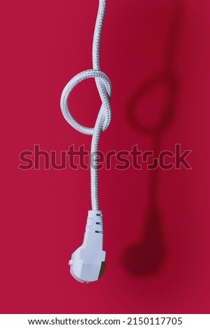 Electric plug for a socket with a knot on a cable on a red background. The concept of the inability to get energy or electricity. Electric plug without socket. No access to electricity or power outage