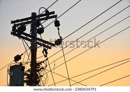 An electric pole surrounded by tangled cables, set against the backdrop of a beautiful sunset sky.