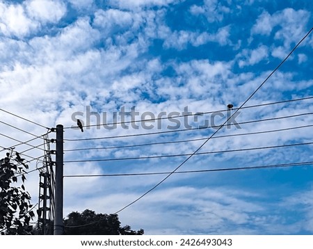 Electric pole and electric wires against beautiful cloudy blue sky background. Many glowing clouds spreading on the deep blue sky in daylight. Multitude soft white fluffy clouds covered the blue sky