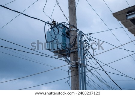 electric poles with transformers and cables attached. The electricity pole is high, has many wires attached and a black cloud background.
