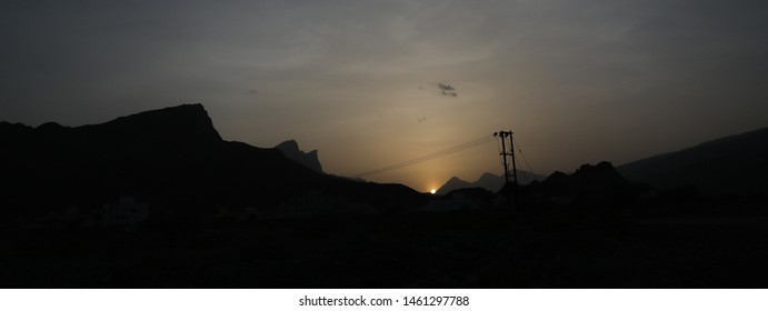 Electric poles and wires extend with sunset behind the high mountains of Oman