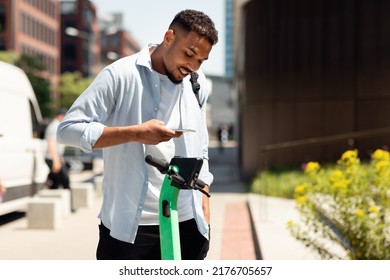 Electric push scooter sharing services. Young black guy renting motorized kick e-scooters in the city, paying online with smartphone. Urban lifestyle