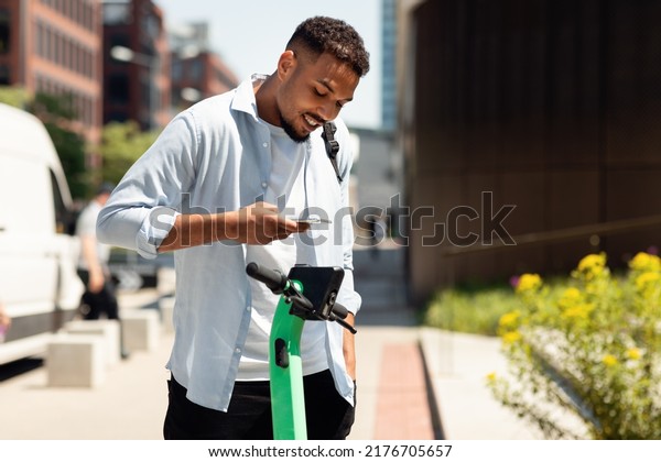 Electric push scooter sharing services. Young\
black guy renting motorized kick e-scooters in the city, paying\
online with smartphone. Urban\
lifestyle