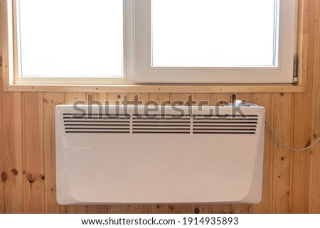 Electric radiator under the window of a country house whose walls are finished with clapboard