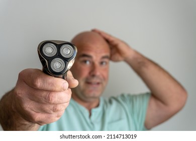 Electric razor in the hand of a Caucasian man with a shaved head. - Shutterstock ID 2114713019