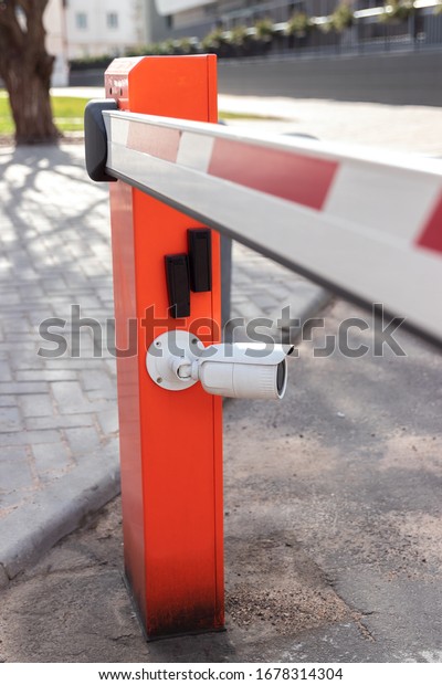 electric red barrier for autos\
in the parking lot with a surveillance camera for reading a car\
number