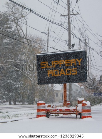 Electric road traffic mobile sign by the side of a snow covered road in winter with snow falling warning of slippery roads