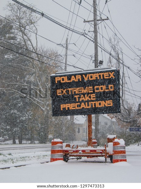 Electric road traffic mobile sign by the side\
of a snow covered road with snow falling warning of polar vortex,\
extreme cold take\
precautions