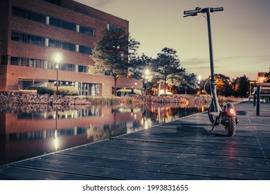 Electric Scooter On A Wooden Pier By The Water At Night.