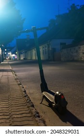 Electric Scooter Parked On The Road At Night.