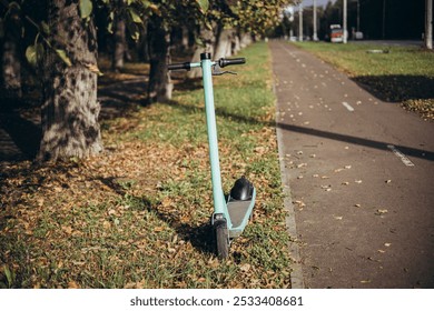 Electric scooter parked on the road of the autumn alley on a background of trees. Electric scooter by autumn park, ecological transport. The concept of eco-friendly urban transport, scooter rental. - Powered by Shutterstock