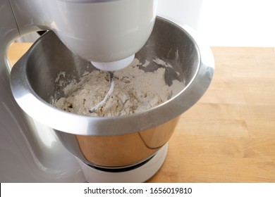 Electric Stand Mixer Is Stirring Dough With The Dough Hook In A Steel Bowl On A Wooden Kitchen Worktop, Baking At Home, Copy Space, Selected Focus, Narrow Depth Of Field