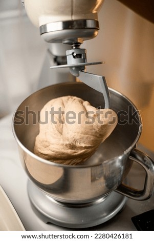Electric stand mixer is stirring dough with the dough hook in a steel bowl. Close-up