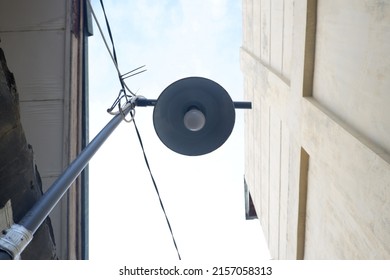 Electric street lamp with poles and wires cables on blue sky. Street lamp with wall view. Street lighting intersected by wires. Photo of a street lamp against a blue sky.