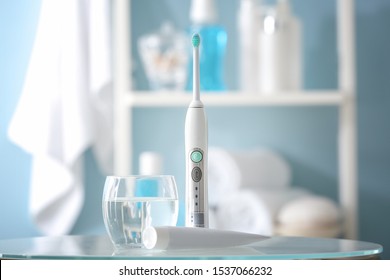 Electric toothbrush with paste and glass of water on table in bathroom