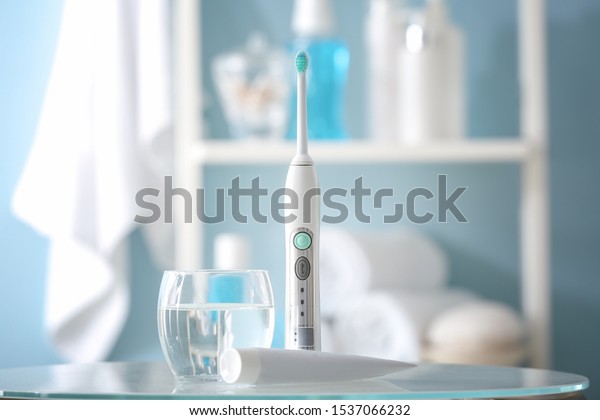 Electric toothbrush with paste and glass of\
water on table in\
bathroom
