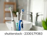 Electric toothbrushes in glass holder indoors, closeup. Space for text