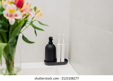 Electric Toothbrushes On A Black Stand With A Black Soap Dispenser In The Bathroom